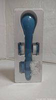 Blue body scrubber with three interchangeable brush heads and USB charging cable in white plastic packaging shown from front view.