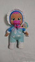 Front view of Cry Baby Tears doll dressed in blue and white plush outfit, bonnet, and attached pacifier.