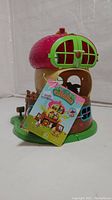 Front and side view of Li'l Woodzeez Acorn Treehouse showing the red acorn top with green window shutters, brown base, and included tags.