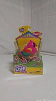Front-facing image of Little Live Pets Lil' Bird in original package, showing bright pink and yellow bird with interactive features highlighted on box