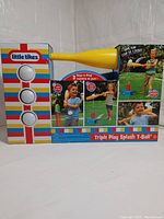 Front view of boxed Little Tikes Triple Play Splash T-Ball set showing yellow bat, colorful target stand with buttons, and images of kids playing outdoors with water feature and bat.