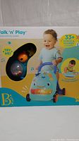Front of the box showing the baby activity walker with 33+ songs, sounds and lights, and a toddler playing with it.