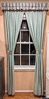 Full view of one window with closed green blackout curtains, floral and geometric patterned valance and matching tiebacks.