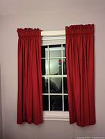 Full view of installed red blackout curtains on window showing gathered top and length nearly touching floor.
