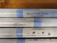 Four rolls of Designer Guild wallpaper with blue and white stripes and labels showing brand name, design name (JALI), part number (P.203-03), batch number (T.17), and provenance (European Community).