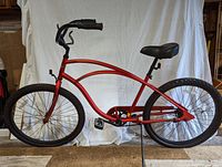 Full side profile of red Electra beach cruiser bicycle showing frame style, tires, seat, handlebars, and pedals.