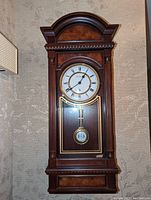 Front view of wooden grandmother clock with glass door showing clock face and pendulum.