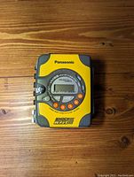 Front view showing yellow and gray Panasonic Shock Wave RQ-SW20 cassette player with digital display and multiple orange function buttons.