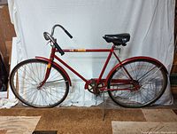 Side profile of the vintage Columbia Roadster bicycle showing the left side with red frame, black saddle, chrome handlebars, and front wheel.