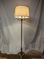Full view of the vintage brass colored floor lamp with a beige drum shade and its lighting arrangement.