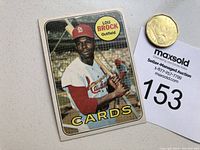 Photo of front of the Lou Brock baseball card shown next to a coin and auction tag for scale.
