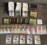 Stacks of loose cards including hockey players, teams, and logos laid out with multiple unopened Panini sticker packs with black and colored design, plus scattered duplicates.