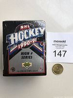 Front view of sealed 1990-91 Upper Deck NHL Hockey Card High # Series box with visible shrink wrap and a coin for scale.