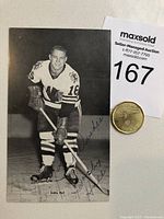 Front view of the black and white postcard showing Bobby Hull in hockey uniform holding a stick with blue ballpoint autograph.