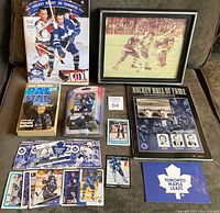 Entire memorabilia lot showing programs, autograph holder, sealed Zamboni toy with Eric Lindros card, framed photo of Darryl Sittler, 20 assorted Toronto Maple Leafs hockey cards, and books about team and Hall of Fame.