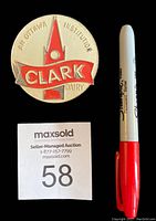 Front view of the vintage Clark Dairy pin showing red enamel and metal with text and logo.