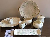 All eight pieces arranged on table including large handled dish on stand, rectangular tray, two mugs, creamer, sugar bowl, and lidded jar.