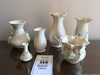Front view of all six Belleek porcelain vases grouped on a surface showing variety of shapes and floral decorations.