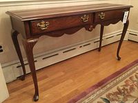 Full side view of the wooden console table showing its shape, drawers, and brass handles