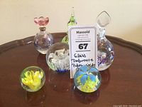 Seven decorative glass pieces on wooden table: four spherical paperweights with floral designs and three clear glass perfume bottles with decorative stoppers.
