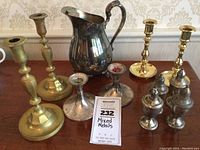Photo showing entire collection of brass candlesticks, silver plate weighted candlesticks, sterling salt and pepper shakers, and sterling weighted pitcher together on table with label 'Mixed Metals'
