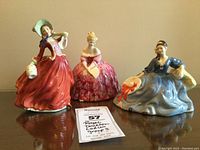 Three figurines on mirrored surface with lot tag visible