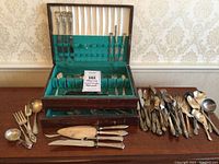 Overall view of wooden chest on table with flatware pieces both in chest and loose on either side