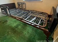 Full view of adjustable hospital bed frame with side side guardrails, resting on green carpet in a room.