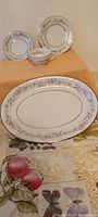 Photo showing two round plates, a small bowl, and an oval serving platter with floral pattern and gold trim, displayed on a cloth with fruit and butterfly design