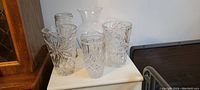Photo showing five lead crystal vases with distinct cut glass designs arranged on a white surface.