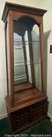 Full view of the front and side of the wood display cabinet showing glass shelves and bottom storage doors.