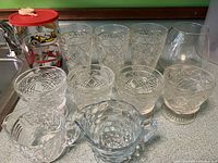 Front view of all vintage glassware pieces including drinking glasses, bowls, creamer, and container with lid.