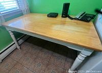 Rectangular kitchen table with natural wood butcher block top and white painted spindle legs, placed against green wall near window.