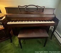 Photo of upright dark wood piano with closed lid and duet bench in front
