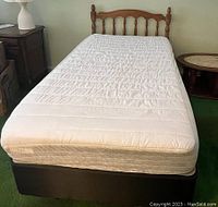 Twin bed with wooden spindle headboard, white quilted mattress on top, black box spring underneath.