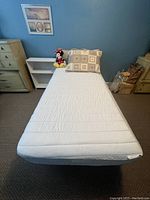Twin size bed setup with metal frame, white headboard, mattress, pillows and stuffed toy in room setting