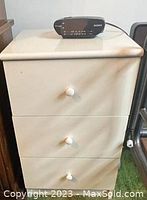 Front view of white wooden nightstand with three drawers and round knobs. Minor signs of use visible on drawer fronts and top surface.