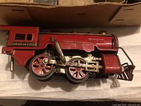 Side view of red metal American Flyer locomotive engine showing wheels, piston rods, and paint wear.