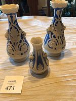 Three blue and white porcelain vases with raised white grape cluster decoration stand on a table.