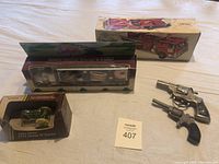 Five collector items displayed including Hess fire truck, Dunkin Donuts tractor trailer, John Deere tractor, and two vintage cap pistols in their original boxes.