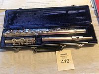 Silver Gemeinhardt flute disassembled in a black hard case with blue velvet interior, showing keys and body parts.