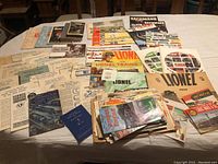 Wide view of the large assortment of Lionel train-related catalogs, instructions, magazines, and handouts spread out on a table.