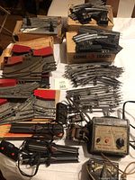 Vintage Lionel train track parts including electric switches, remote controls, curved and straight track pieces, transformers, and control devices arranged on a table.