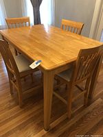 Full view of high dining table with four matching wooden chairs around it.