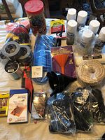 Photo showing cleaning brushes, spray paint cans, duct tape rolls, rope, funnels, and various straps and cords on table