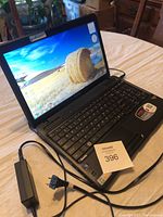 View of Toshiba Satellite laptop powered on displaying a desktop background of a hay bale in a field, with charging cord and adapter next to it.