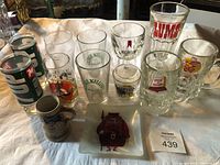 Photo showing various vintage glassware including beer mugs, soft drink glasses, tankard, and decorative plate with brand logos.