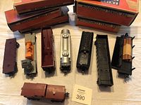 Seven vintage Lionel model train cars placed in a row, accompanied by some original boxes behind them, some with damage.