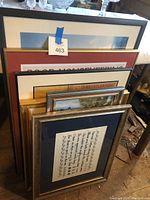 Framed items stacked together showing a variety of frames and art styles including prints, posters, and a mirror