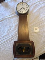 Full view of the wooden wall clock showing dial, case, and pendulum window.